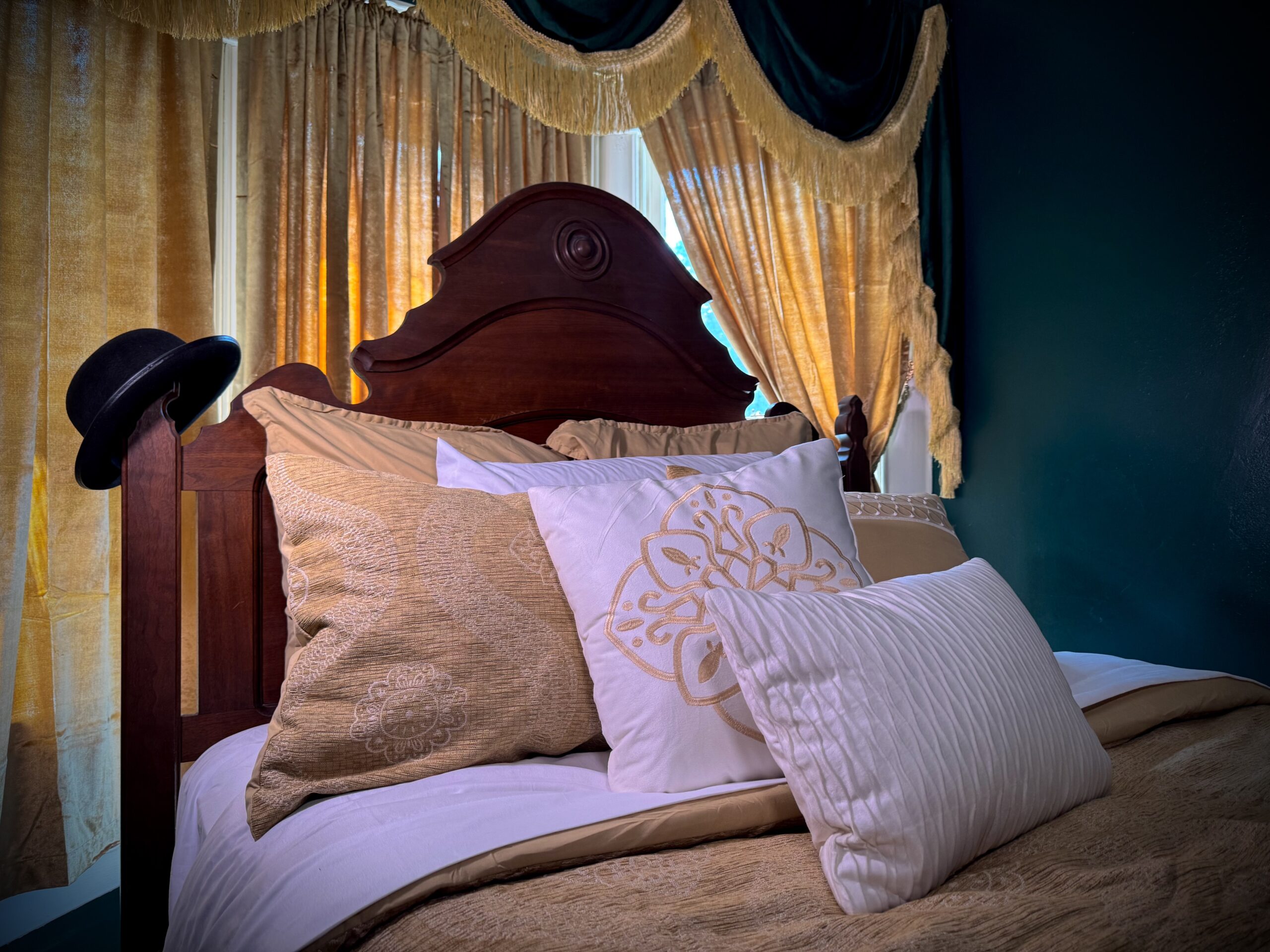 Antique wooden bed dressed in gold and cream linens beneath teal-and-gold drapery in Laura’s Room
