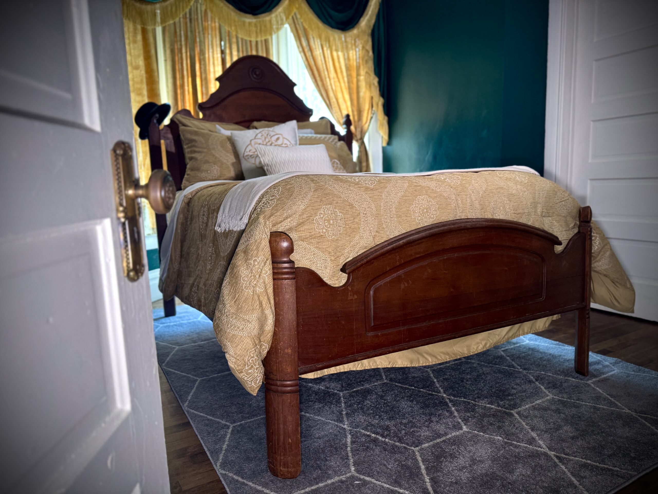 View through the open door into Laura’s Room with an antique wooden bed and teal walls at Fears House